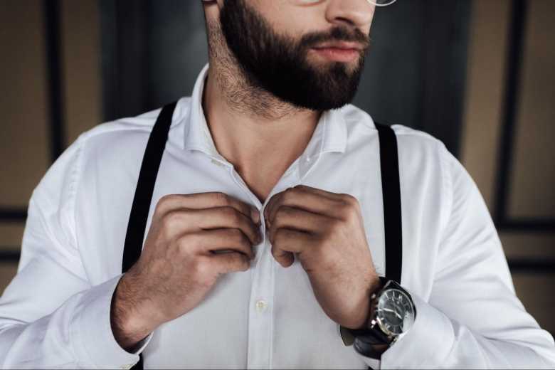 Man with a Beard buttoning Up his Shirt and Wearing Suspenders