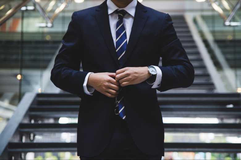 A close up image of a man in a black suit buttoning up his jacket