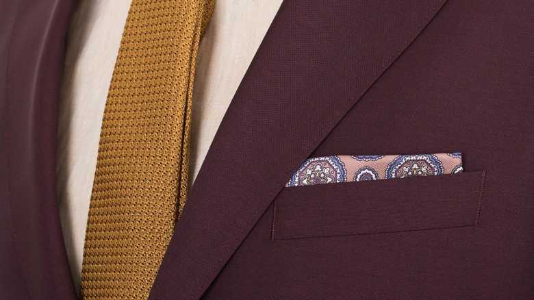 a close-up shot of a marron suit, accessorized with a yellow tie and a patterned handkerchief by Oliver Wicks