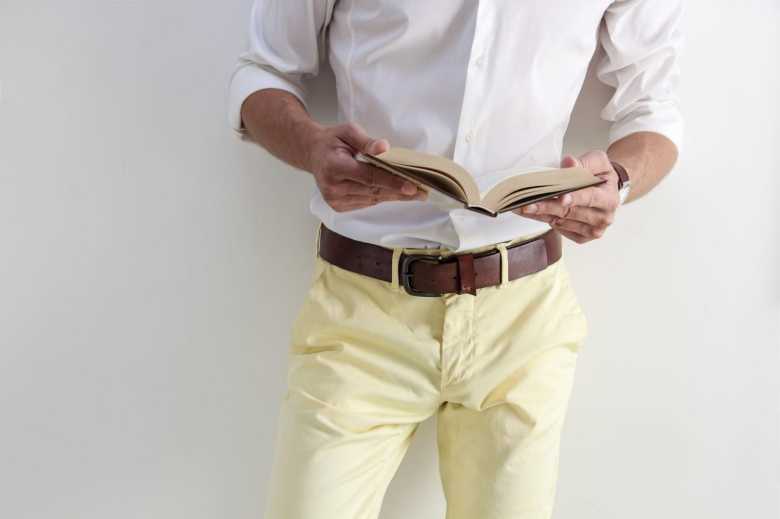 Man's Torso wearing Yellow Pants and  Brown Belt Reading a Book