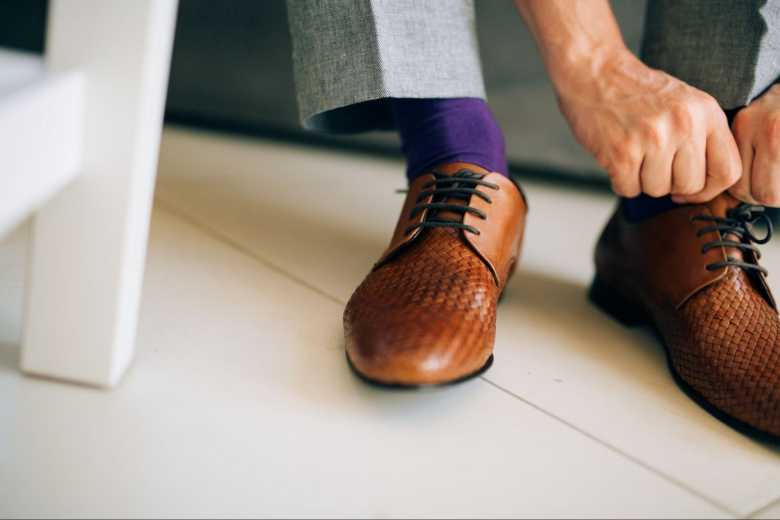 Man Tieing his Shoelaces Wearing Grey Suit Pants, Brown Shoes and Purple Socks