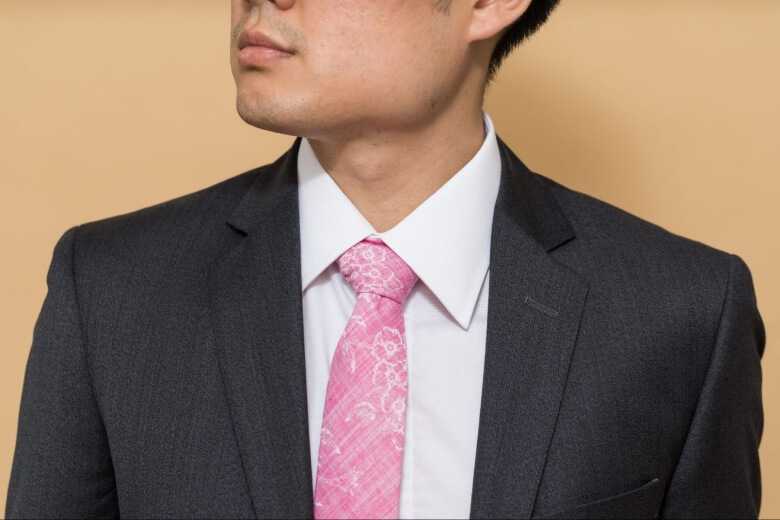 a close-up shot at a man wearing a black costume with a pink tie